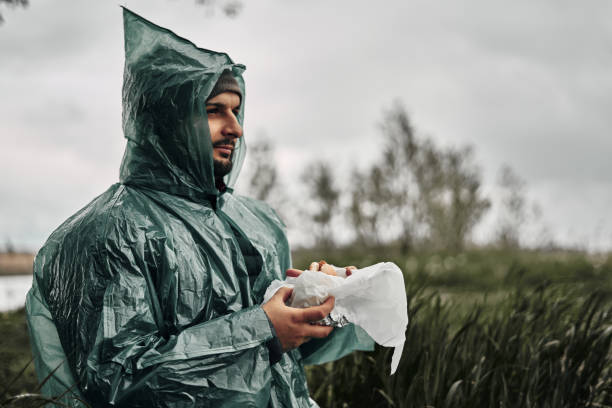 ein mann mit bart im grünen regenmantel isst in der natur. bewölktes wetter, fast food. - 11320 stock-fotos und bilder