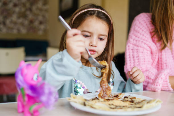 frontansicht auf kleine kaukasische mädchen essen pfannkuchen wüste im restaurant - kleines kind weibliches kind beim frühstück am tisch zu hause am tag - aufwachsen und essen essen konzept - eierkuchen speise stock-fotos und bilder