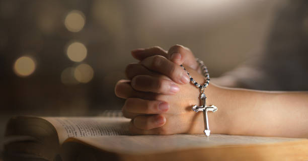 christian religion background with light bokeh christian woman hand on holy bible praying to god holding cross rosary selective focus at cross. concept of christian religious people faith and practise - prayer beads imagens e fotografias de stock