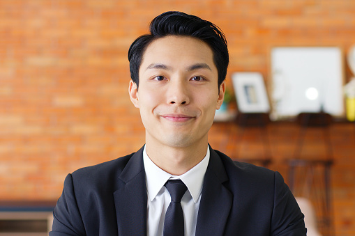 Portrait Young Asian businessman talking on video call or virtual meeting in office, front view, look at camera