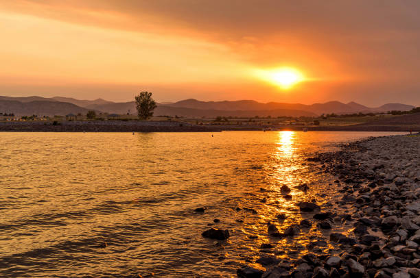 The setting sun shines through thick haze from smoke of several wildfires in Rocky Mountains onto calm water of Chatfield Reservoir. Summer of 2020, Denver-Littleton, Colorado, USA.