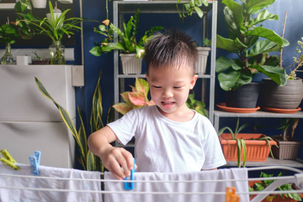 lindo niño asiático divirtiéndose colgando ropa lavada limpia en el tendedero para secar en casa - hang to dry audio fotografías e imágenes de stock