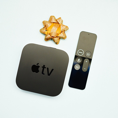 Peyton, Colorado, USA - 28 November 2020: A studio shot of an Apple TV 4K HD box with remote control and a gold gift bow on a pale blue surface.