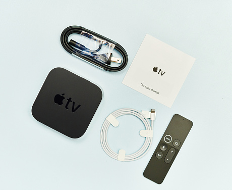 Peyton, Colorado, USA - 28 November 2020: A studio flat lay shot of an Apple TV 4K HD box with remote control and cables on a pale blue surface.