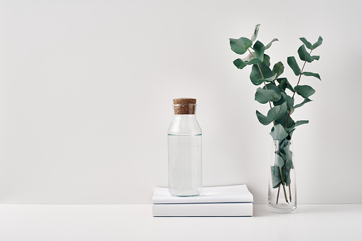 A transparent bottle with a cork stopper and a vase with eucalyptus branches on a white background. Natural and eco-friendly materials in interior decor. Copy space, mock up