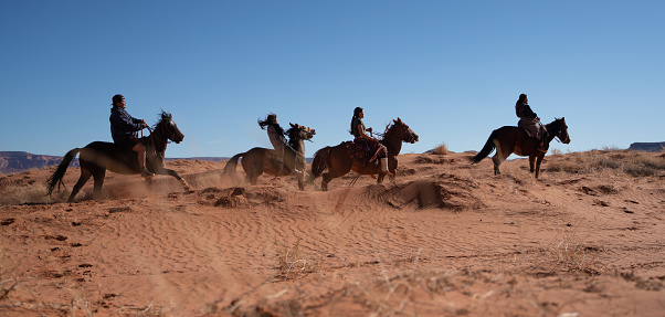 Four Navajo siblings riding horses among the sand dunes in Arizona - USA