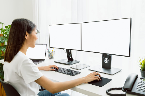 Young Asian woman sitting on chair and working at the computer with blank screen in home on the day light shone in the afternoon.