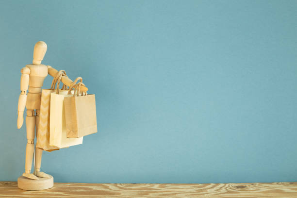 wooden mannequin doll holding paper shopping bags. blue background - puppet craft paper paper bag imagens e fotografias de stock