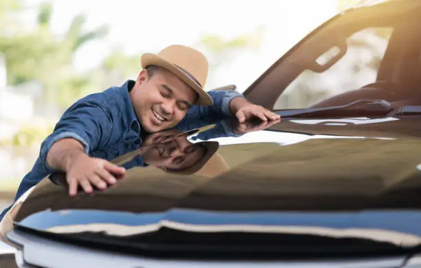 Photo of Young handsome asian man getting the new car. He hugged his car and was very happy. Buy or rent car concept.