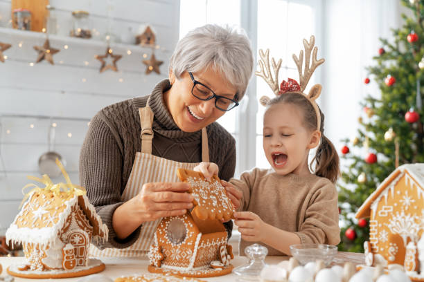 Cooking Christmas food Merry Christmas and Happy Holidays. Family preparation holiday food. Grandmother and granddaughter cooking gingerbread house. tradition stock pictures, royalty-free photos & images