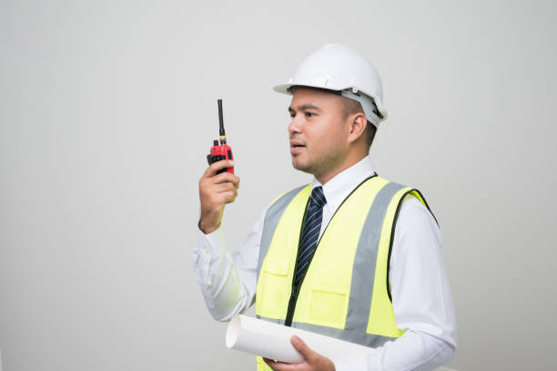 istock Asian civil engineer operate with radio walkie talkie to control working in studio. Worker wearing hard hat standing on isolated white background. 1288556344