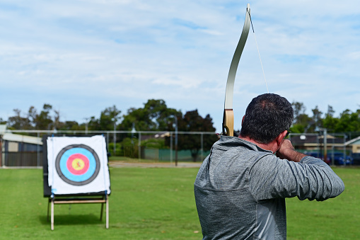 Archer aiming an arrow at a target in outdoor range. Archery is the art, sport, practice, and  skill of using a bow to shoot arrows.