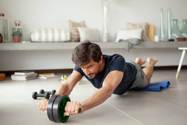 リビングルームで運動する男性 - 腹筋ローラー ストックフォトと画像