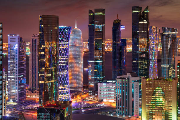 Aerial view down to modern urban skyscrapers in the City of Doha illuminated at Night. Glowing Business Buildings, Hotel, Office Buildings in Downtown Doha. Aerial View of Downtown Doha City, Qatar, Middle East