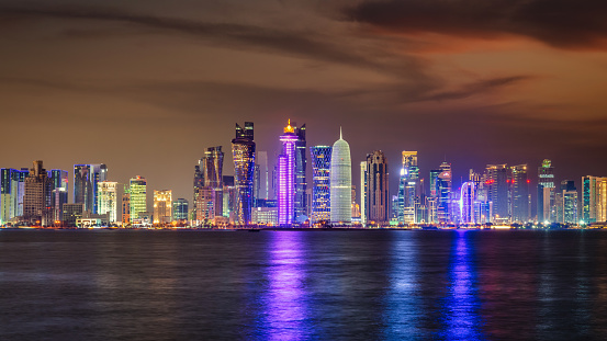 Modern urban skyscrapers of the Cityscape of Doha illuminated at Night. Panorama of the illuminated Business Buildings, Hotel, Office Buildings in Downtown Doha reflecting in the Persian Gulf Water. Cityscape of Downtown Doha, Qatar, Middle East