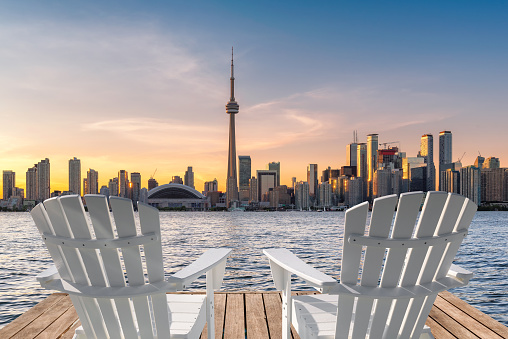 Toronto skyline from wooden pier with white chairs at sunset in Toronto, Ontario, Canada.