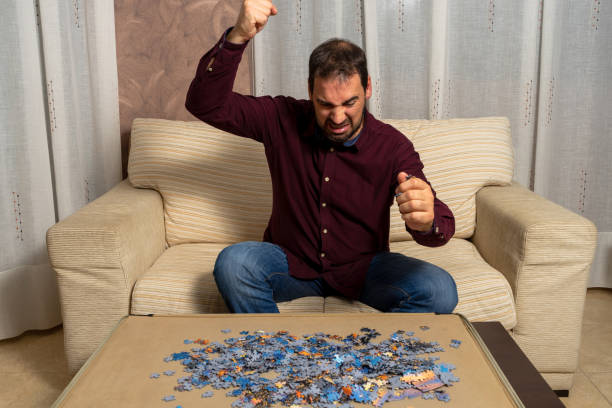 istock Young man with beard sitting on the couch at home doing puzzle 1288565247