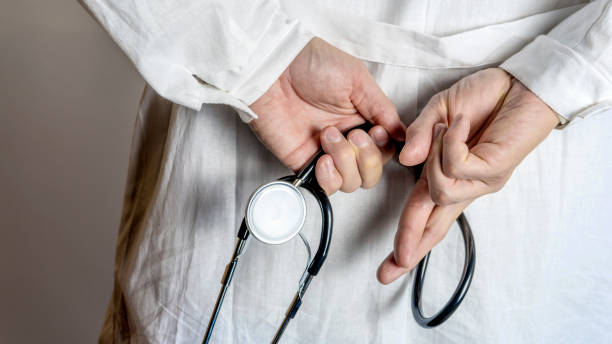 istock Doctor in white coat holds hands behind his back with stethoscope. Close up. 1288565382