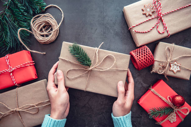 istock Hand holding Christmas gift box and tree branch decor on black background. 1288565544