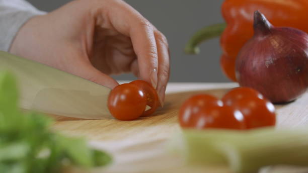 istock Cutting one red cherry tomatoes with kitchen knife on wooden board 1288567556