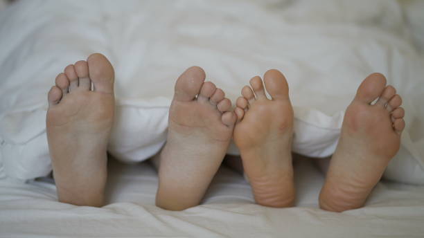 istock Womans feet flirting with man in bed, couple having intimate problem, relations 1288568436