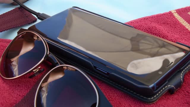 Blurry reflections in sunglasses and smartphone screen atop red towel at beach