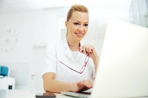 Portrait of handsome smiling blond female laboratory assistant sitting in lab and using laptop for entering test results. Portrait of handsome smiling blond female laboratory assistant sitting in lab and using laptop for entering test results. entering data stock pictures, royalty-free photos & images