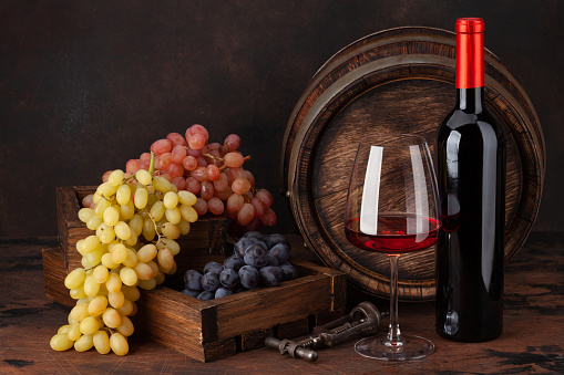 Wine bottle, grapes, glass of red wine and old wooden barrel. With copy space
