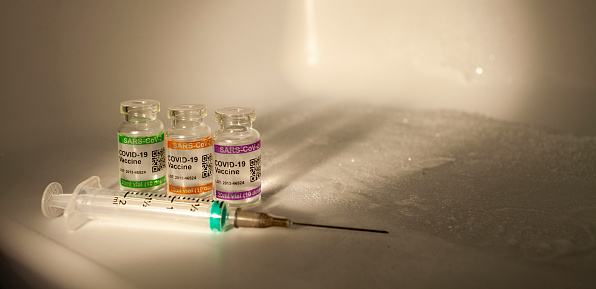 Syringe in close up with set of bottles with COVID-19 (SARS-CoV-2) Coronavirus vaccine vials and injection syringe. Copy space provided.\n\nNote: QR code on bottles was generated by me and contains generic text: \