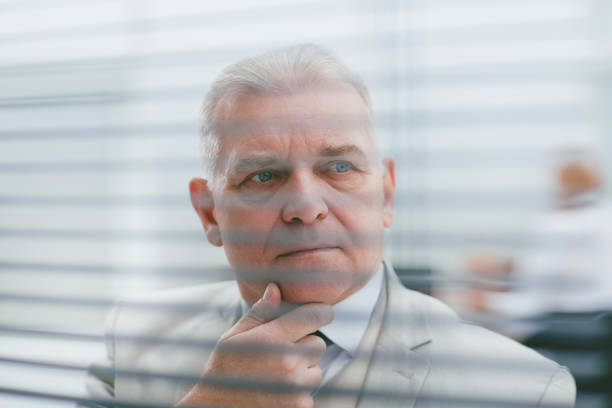 istock close up. brooding elderly businessman standing in front of office window 1288579728
