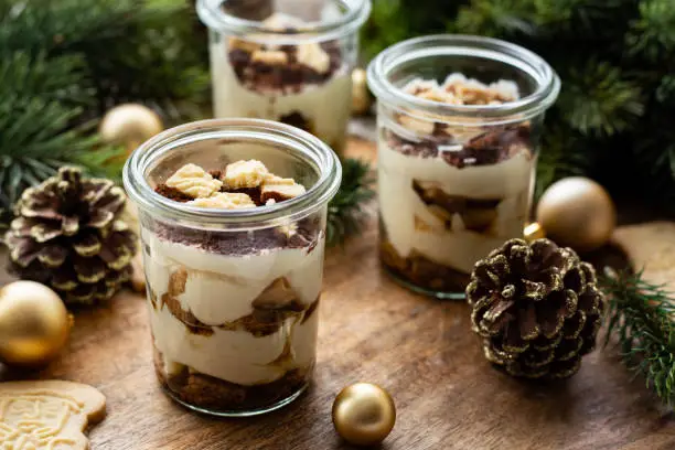Tiramisu with spekulatius in a dessert glass. Close up. Decorated with pine cones, branches and christmas balls. Part of a series