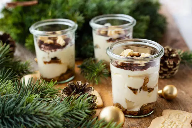 Tiramisu with spekulatius in a dessert glass. Close up. Decorated with pine cones, branches and christmas balls. Part of a series