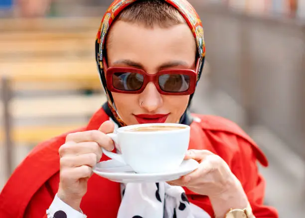 woman in red coat and sunglassess drinking coffe in the citycentre after shopping