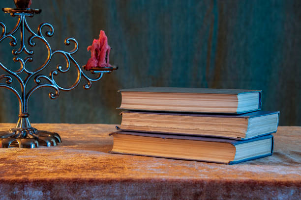 Composition of green burning candle and pile of books against white background
