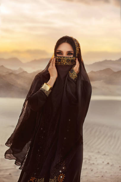Portrait of young beautiful Asian girl. The face of woman is hidden by a veil black scarf. evening make-up, smoky eyes. The head is covered. Traditional dress with gold embroidery. Nature desert retrato de joven hermosa chica oriental. el rostro de la mujer está oculto por una bufanda negra de velo. maquillaje de la noche, ojos ahumados. la cabeza está cubierta. vestido tradicional con bordados dorados. desierto de la naturaleza.