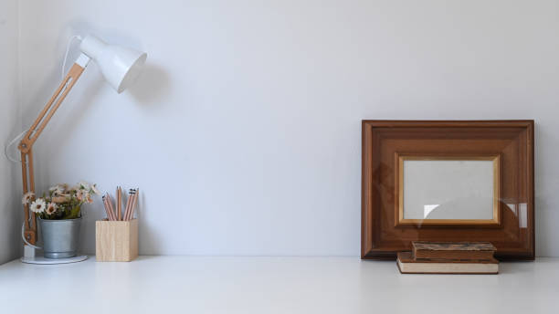 istock Vintage workspace with frame, pencils, pot plant, coffee cup, lamp and old book on white table. 1288600336