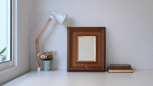 istock Vintage workspace with empty frame, pot plant, lamp and old book on white table. 1288600442