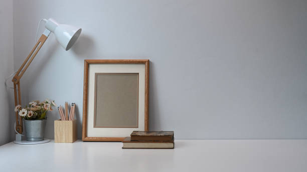 istock Minimal workspace with frame, pencils, coffee cup, lamp and old book on white table. 1288600445