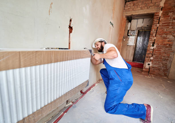 istock Young handsome plumber installing water radiator in unfinished apartment 1288603255