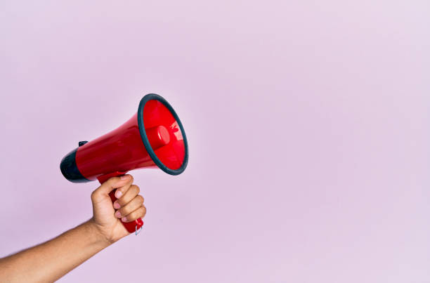 istock Hand of hispanic man holding megaphone over isolated pink background. 1288603676