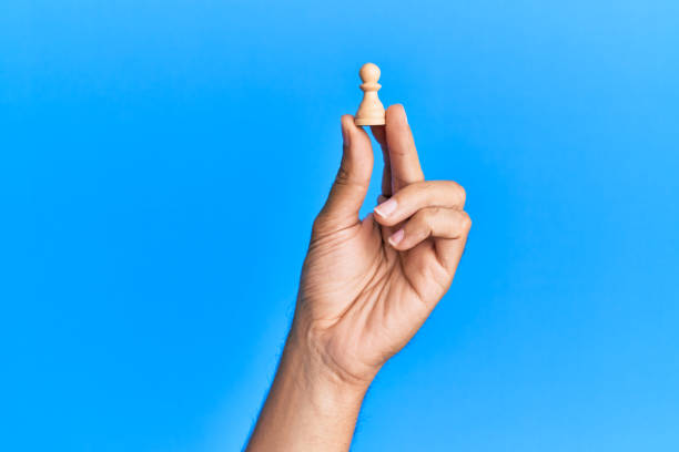 hand of hispanic man holding pawn chess piece over isolated blue background. - board game piece leisure games blue isolated imagens e fotografias de stock