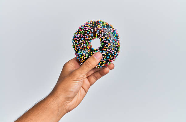 istock Hand of hispanic man holding chocolate donut over isolated white background. 1288604036