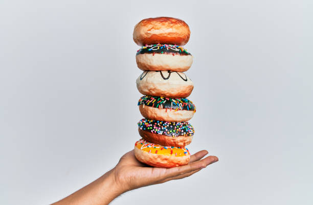 Hand of hispanic man holding tower of donuts over isolated white background. Hand of hispanic man holding tower of donuts over isolated white background. donut stock pictures, royalty-free photos & images