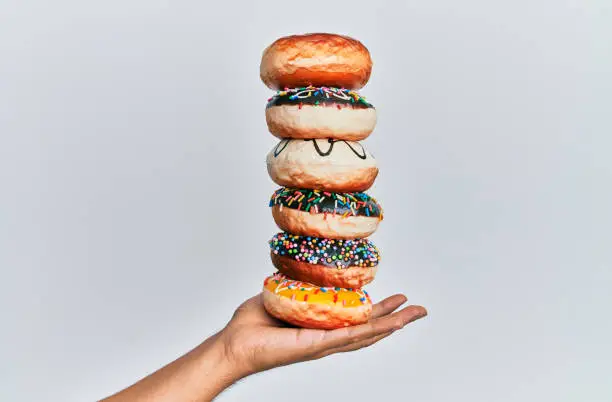 Photo of Hand of hispanic man holding tower of donuts over isolated white background.