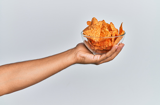 Hand of hispanic man holding bowl with mexican nachos potatoes over isolated white background.