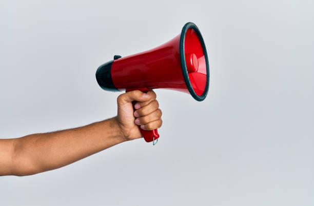 istock Hand of hispanic man holding megaphone over isolated white background. 1288604827