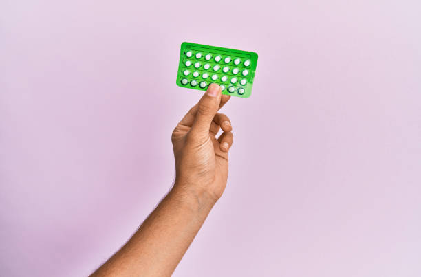 young hispanic hand holding birth control pills over isolated pink background. - contraceção imagens e fotografias de stock