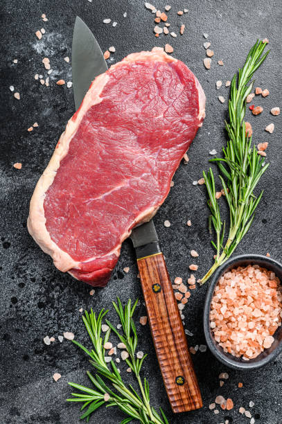 Raw New York steak or striploin with herbs. Black background. Top view Raw New York steak or striploin with herbs. Black background. Top view. barbecue beef stock pictures, royalty-free photos & images