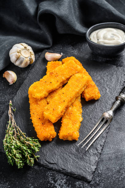 istock Oven baked crumbed fish sticks made from white fish.  Black background. Top view 1288606603