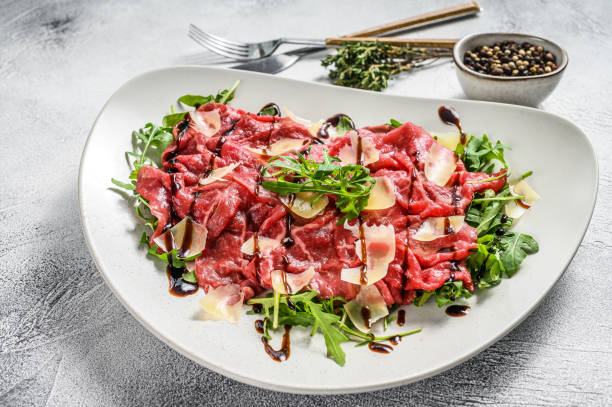 Italian Beef carpaccio with arugula salad, parmesan cheese. Gray background. Top view Italian Beef carpaccio with arugula salad, parmesan cheese. Gray background. Top view. carpaccio parmesan cheese beef raw stock pictures, royalty-free photos & images